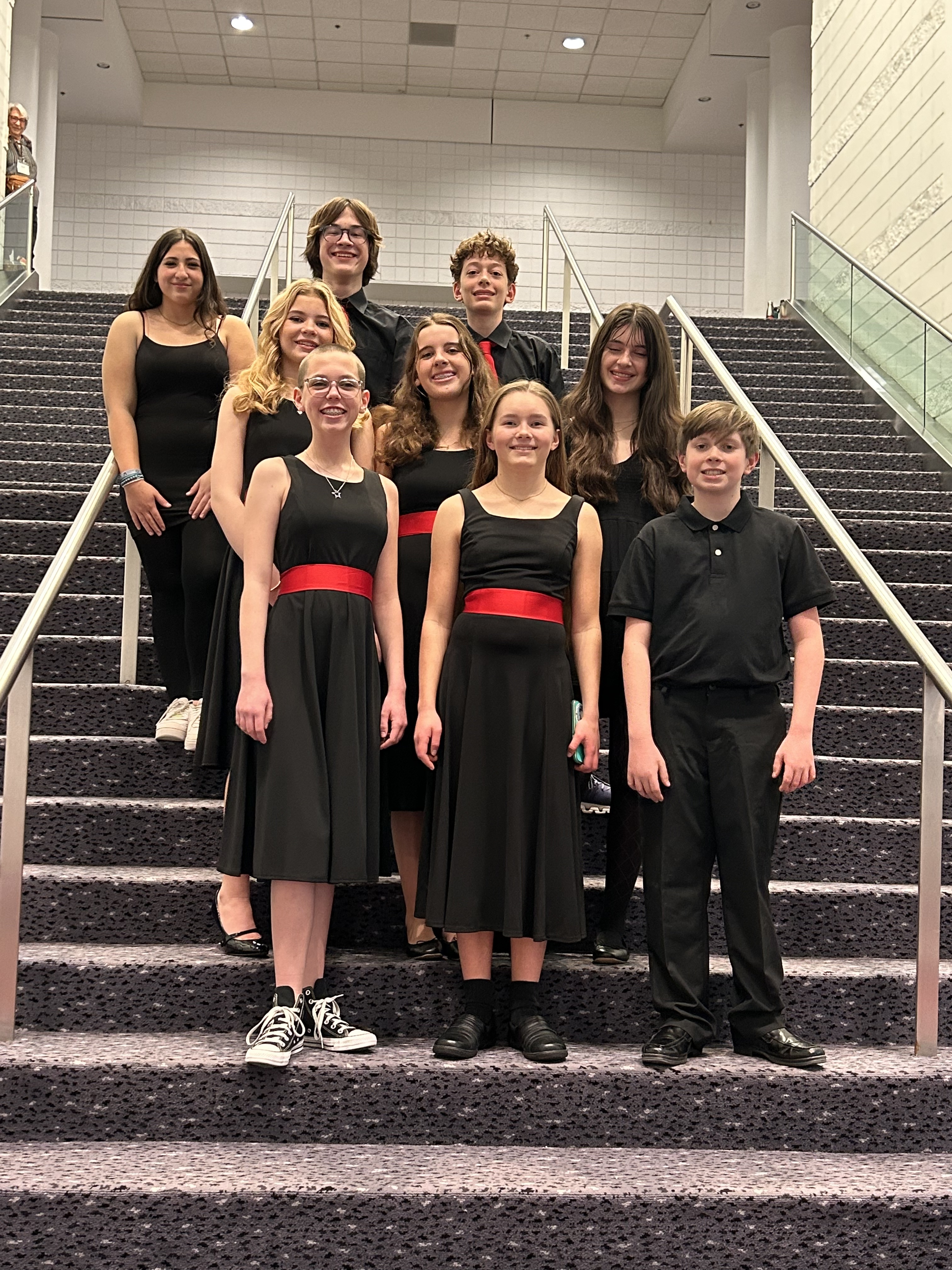 Nine choir students, a mix of male and female, stand on stairs