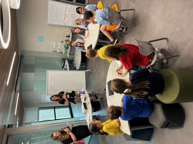 Two elementary school teams sit in a pod common area at Ford Elementary while two middle school students read trivia questions for them.