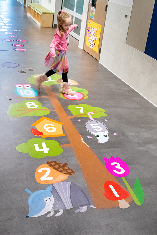 image: elementary girl playing hopscotch in school hallway