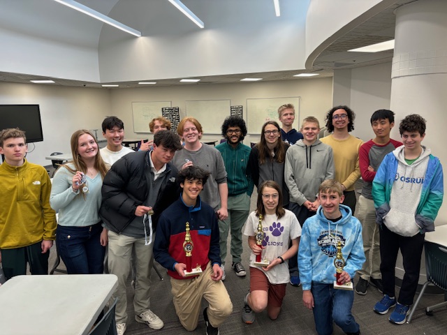 A group photo of participants in the LPS high school chess tournament with winners in the front row with their trophies.