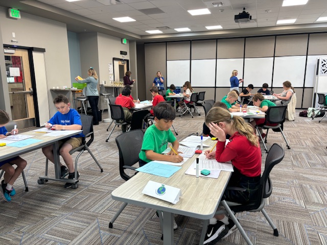 Students working at a table on a math written test in a room hosting the district math tournament
