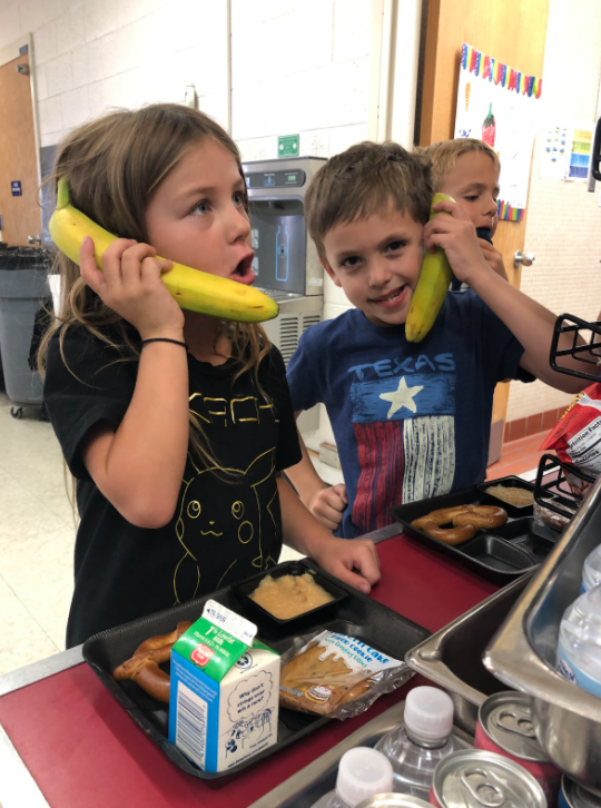 Students in lunch line, holding bananas like phones