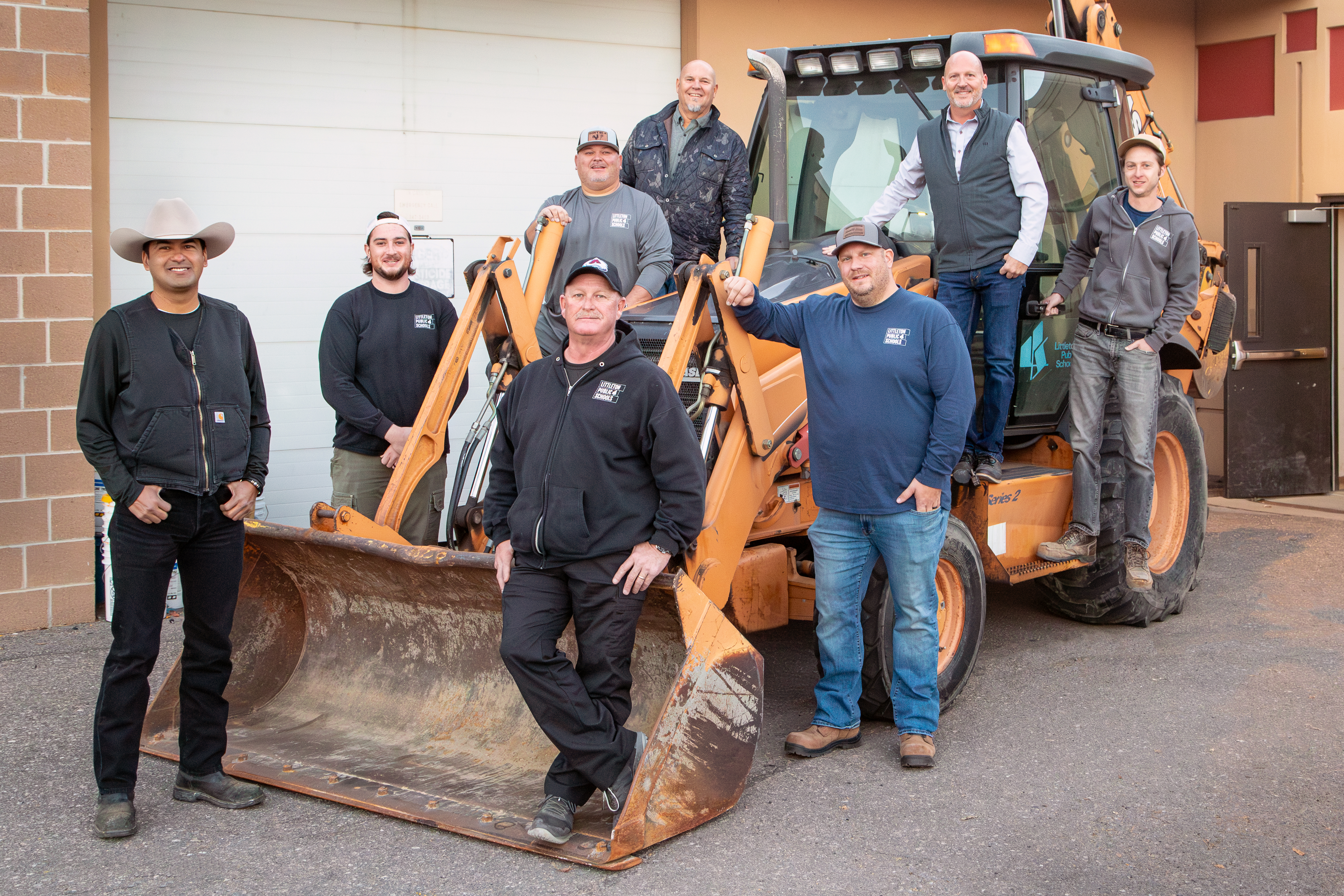 Operations and Maintenance Crew of 8 posed on a parked backhoe