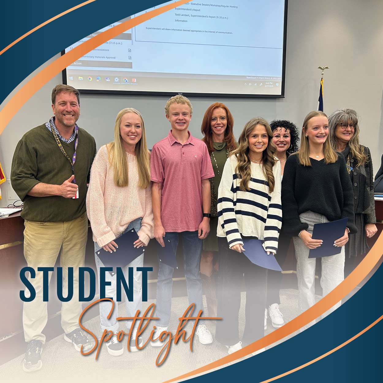 Four students stand with the Board of Education in the boardroom. The students are holding certificates and smiling; they are dressed casually in various outfits, including a pink shirt, a striped sweater, and a black sweater. The adults, dressed professionally, are smiling, with one man giving a thumbs-up. The background shows a projector screen and a Colorado state flag. The image includes a graphic overlay with the words "STUDENT Spotlight" in bold blue and orange text, surrounded by curved design elements in blue and orange.