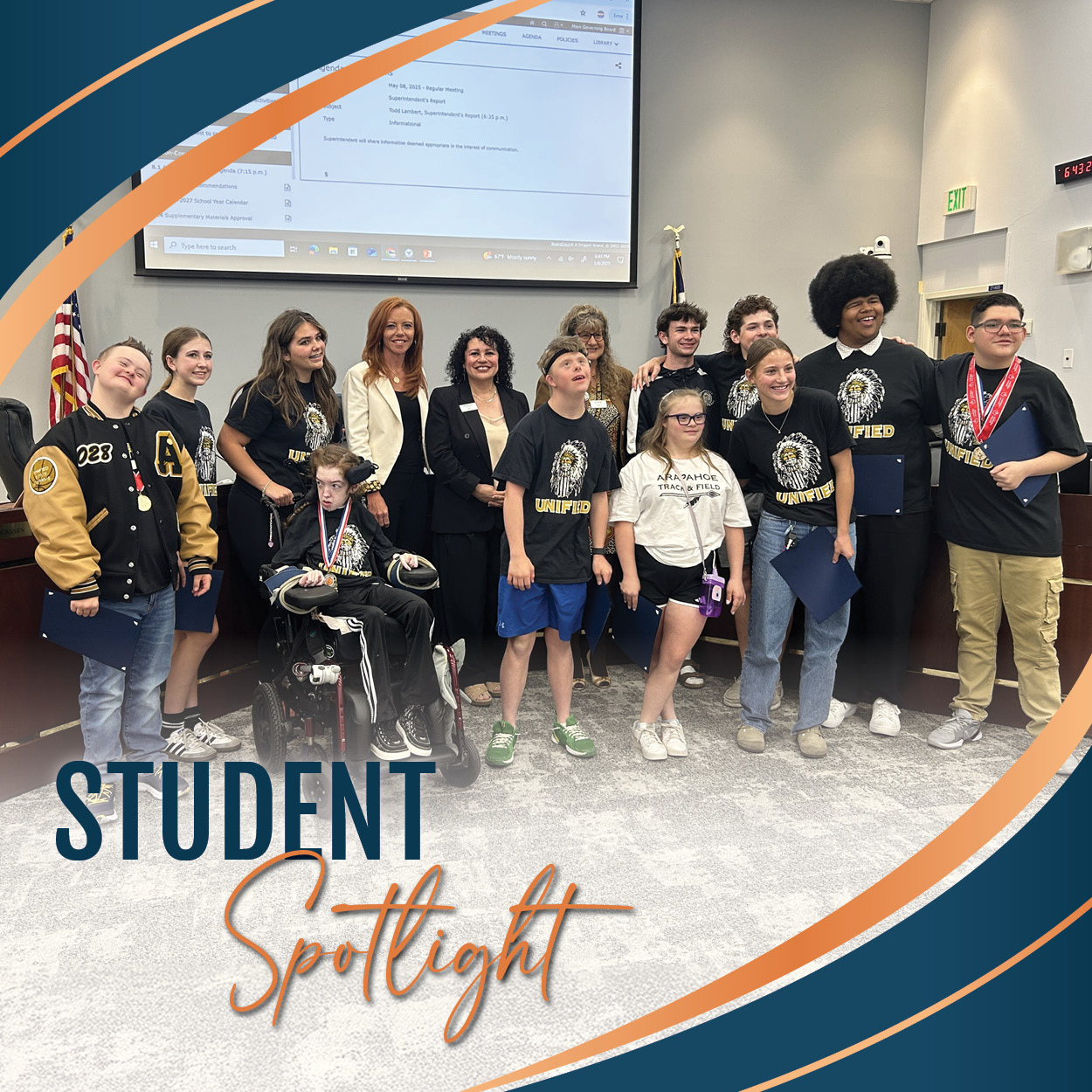 Group photo of Arapahoe High School's Unified Basketball Team and several adults at a Board of Education meeting. Students of diverse backgrounds and abilities are smiling, with one student in a wheelchair and others wearing medals and holding certificates. Most are wearing black "Unified" shirts featuring the school's logo. The image is framed with curved navy blue and orange lines, with the text "Student Spotlight" at the bottom left.