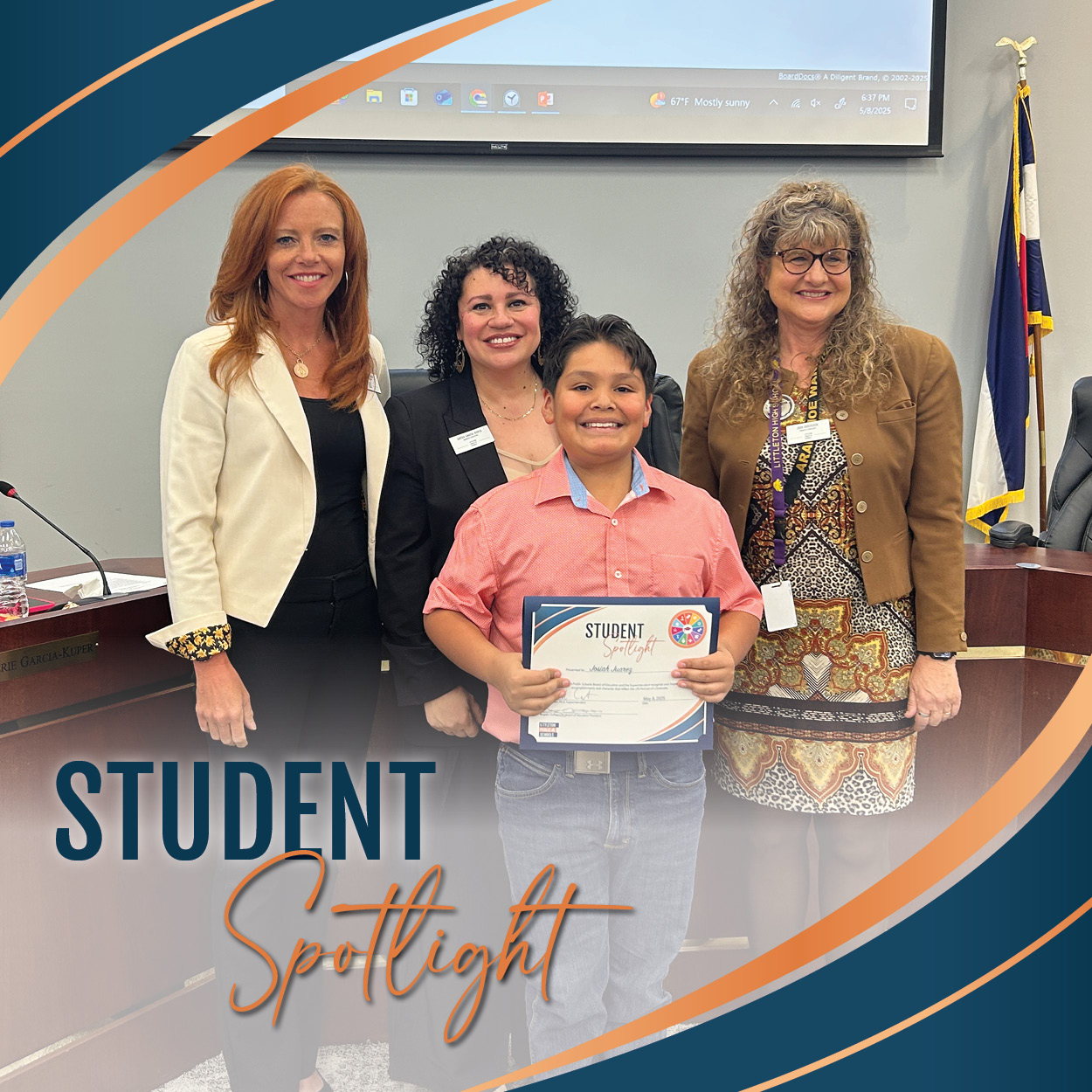 An elementary school student stands smiling and holding a Student Spotlight certificate at a Board of Education meeting. He is wearing a salmon pink button-up shirt and jeans. Three professionally dressed women stand behind him, also smiling. Behind them is a projection screen, part of the boardroom setup, and a visible U.S. and Colorado flag. The image includes a curved graphic border in navy blue and orange, with the words “Student Spotlight” in stylized text at the bottom left.