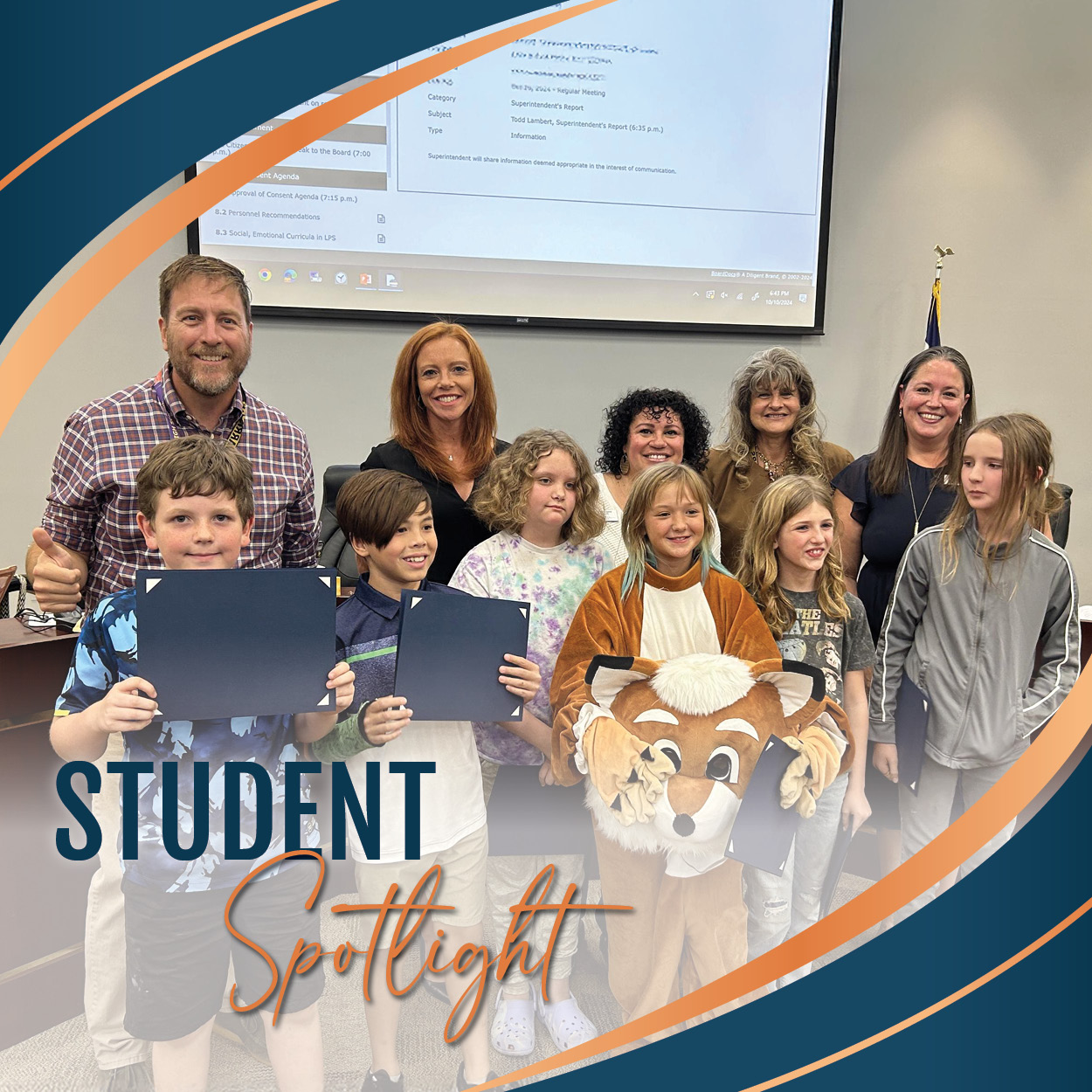 A group of elementary-aged students standing proudly with certificates, along with one student wearing the Ford Fox mascot costume. They are joined by smiling Board of Education members, who are standing behind them in support. The setting is an LPS Board of Education meeting, with a presentation screen visible in the background displaying meeting details. The students are being recognized for their achievements, as highlighted by the design overlay text "Student Spotlight" at the bottom of the image. The atmosphere is celebratory and encouraging.